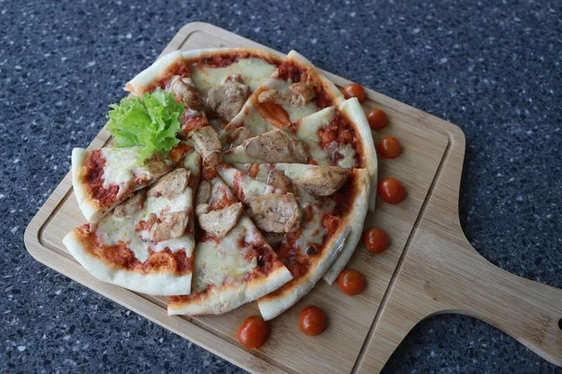 Wood-fired chicken pizza with cherry tomatoes on a wooden board at The Summit Kandy
