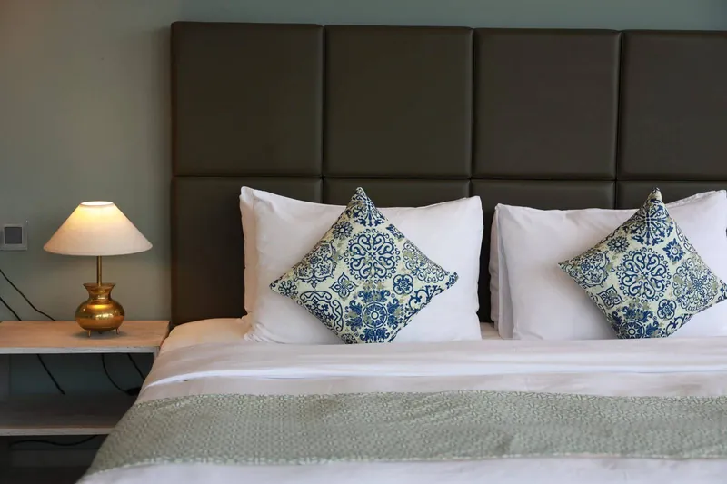 King bed with decorative cushions and a bedside lamp in a guest room at The Summit Kandy
