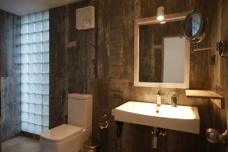 En-suite bathroom with rustic wood-panel walls, toilet, washbasin and mirror at The Summit Kandy