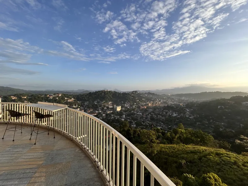 Rooftop terrace with bar seating and curved railing overlooking Kandy city and hills by day at The Summit Kandy